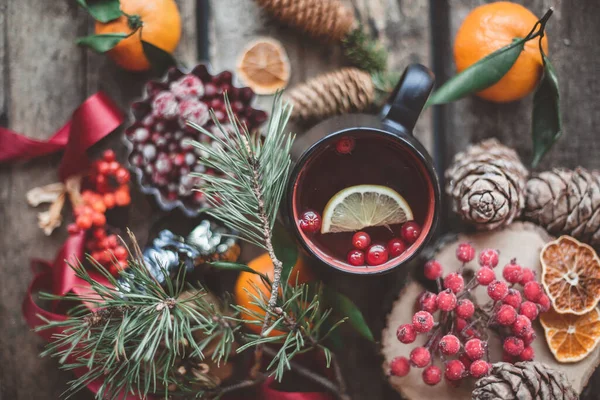 Limonlu sıcak çay, kızılcık. Ahşap arka planda köknar ağacı dalları, mandalina, koni ve berrelerle süslenmiş. Üst Manzara. Kış Noel sıcak içeceği