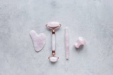 Pembe Gua Sha yüz masajı ve yüz bakımı aletleri. Rose Quartz yeşim taşı, değnek, mantar şekli ve gri arka planda taş. Evde reşit olmama, kaldırma ve tonlama tedavisi. üst görünüm Boşluğu kopyala.