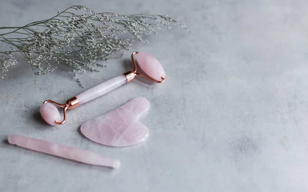 Pembe Gua Sha yüz masajı ve yüz bakımı aletleri. Rose Quartz yeşim taşı, gri arka planda değnek ve taş. Evde reşit olmama, kaldırma ve tonlama tedavisi. üst görünüm Boşluğu kopyala.