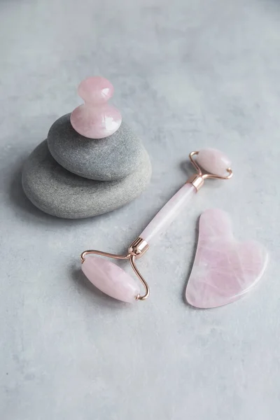 Pembe Gua Sha yüz masajı ve yüz bakımı aletleri. Rose Quartz Yeşim Taşı, gri beton zemin üzerinde mantar şekli ve taş ve gri taş piramit. Yaş, yüz yogası, kaldırma ve tonlama tedavisi