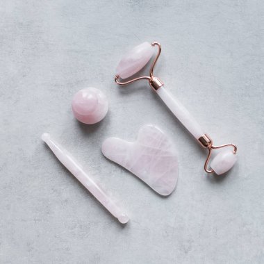 Pembe Gua Sha yüz masajı ve yüz bakımı aletleri. Rose Quartz yeşim taşı, değnek, mantar şekli ve gri arka planda taş. Evde reşit olmama, kaldırma ve tonlama tedavisi. üst görünüm Boşluğu kopyala.