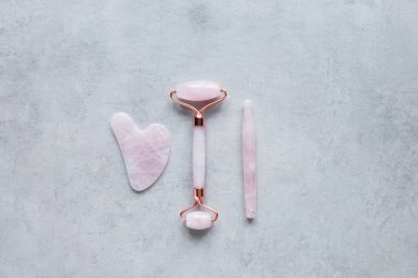 Pembe Gua Sha yüz masajı ve yüz bakımı aletleri. Rose Quartz yeşim taşı, gri arka planda değnek ve taş. Evde reşit olmama, kaldırma ve tonlama tedavisi. üst görünüm Boşluğu kopyala.