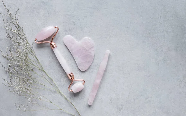 Pembe Gua Sha yüz masajı ve yüz bakımı aletleri. Rose Quartz yeşim taşı, gri arka planda değnek ve taş. Evde reşit olmama, kaldırma ve tonlama tedavisi. üst görünüm Boşluğu kopyala.