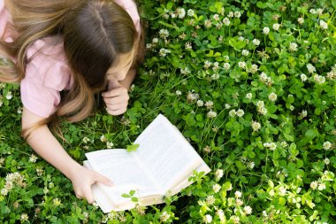Güzel bir kız yüzüstü yatar ve parkta bir kitap okur. Yukarıdan görüntüle