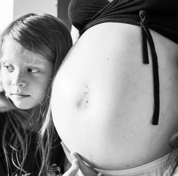 Niño con el pelo largo abraza el vientre de una madre embarazada. — Foto de Stock