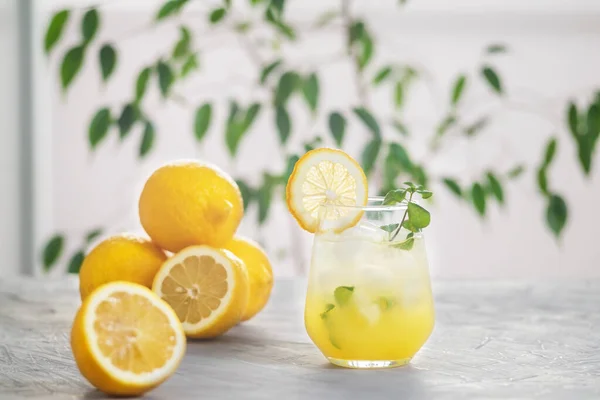 Citronnade glacée aux agrumes dans le verre avec tranche de citron et feuilles de menthe décoration sur table en marbre sur fond naturel — Photo