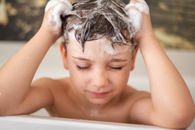 Küçük çocuk banyo banyosunda başını yıkıyor ve gözlerini kapıyor. Çocuklar için şampuan köpüğü