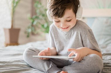 Mutlu çocuk evde yatakta yatıp bilgisayarla oynuyor ya da internetten kitap okuyor ve müzik dinliyor.