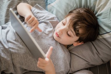 Mutlu çocuk evde yatakta yatıp bilgisayarla oynuyor ya da internetten kitap okuyor ve müzik dinliyor.