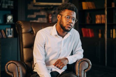 Şık, siyah, beyaz gömlekli, iş yerinde oturan Afro-Amerikan çekici adamın portresini kapat.