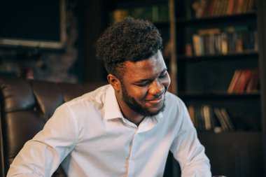 Şık, siyah, beyaz gömlekli, iş yerinde oturan Afro-Amerikan çekici adamın portresini kapat.