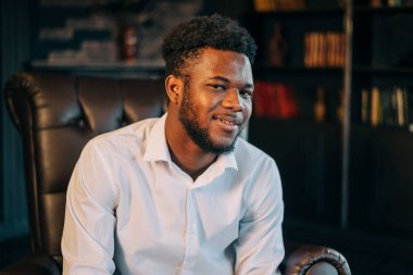 Şık, siyah, beyaz gömlekli, iş yerinde oturan Afro-Amerikan çekici adamın portresini kapat.