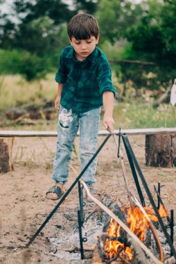 Küçük çocuk orman gezisinde nehir kıyısında şenlik ateşi yakıyor.