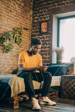 Zenci adam cep telefonuyla mesaj atıyor. Evdeki yatağın üzerinde oturuyor.