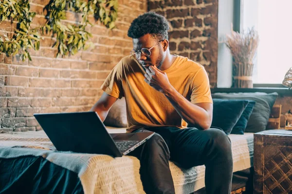 Young attractive black man working at home indoors with computer laptop. IT professions online