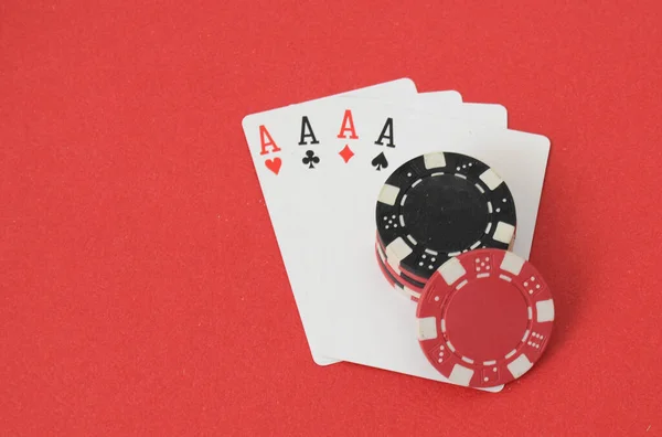 Kırmızı zemin üzerinde dört as ve poker fişleri kazanan bir el..