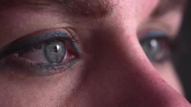 Karanlık odadaki kişinin mavi yeşil gözündeki yansıma.