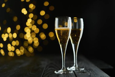 Yeni yılı kutlamak için iki bardak köpüklü şarap ya da şampanya, Mutlu Noeller ya da Bokeh efektli yıldönümü. Şarabın sarısı ve ışıkları koyu bir arkaplanda duruyor..
