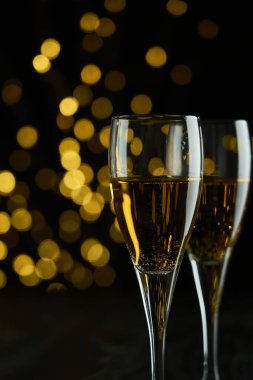 Yeni yılı kutlamak için iki bardak köpüklü şarap ya da şampanya, Mutlu Noeller ya da Bokeh efektli yıldönümü. Şarabın sarısı ve ışıkları koyu bir arkaplanda duruyor..