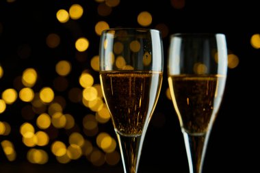 Yeni yılı kutlamak için iki bardak köpüklü şarap ya da şampanya, Mutlu Noeller ya da Bokeh efektli yıldönümü. Şarabın sarısı ve ışıkları koyu bir arkaplanda duruyor..