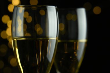 Yeni yılı kutlamak için iki bardak köpüklü şarap ya da şampanya, Mutlu Noeller ya da Bokeh efektli yıldönümü. Şarabın sarısı ve ışıkları koyu bir arkaplanda duruyor..
