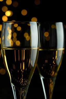 Yeni yılı kutlamak için iki bardak köpüklü şarap ya da şampanya, Mutlu Noeller ya da Bokeh efektli yıldönümü. Şarabın sarısı ve ışıkları koyu bir arkaplanda duruyor..