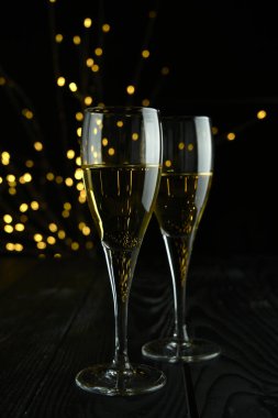 Yeni yılı kutlamak için iki bardak köpüklü şarap ya da şampanya, Mutlu Noeller ya da Bokeh efektli yıldönümü. Şarabın sarısı ve ışıkları koyu bir arkaplanda duruyor..