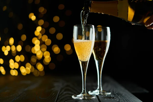 Two glasses of sparkling wine or champagne to celebrate New Year, Merry Christmas or Anniversary with a bokeh effect background. The yellow of the wine and lights stand out against a dark background.