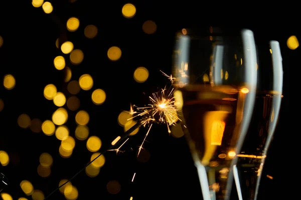 Two glasses of sparkling wine or champagne to celebrate New Year, Merry Christmas or Anniversary with a bokeh effect background. The yellow of the wine and lights stand out against a dark background.