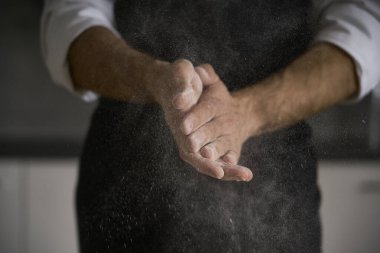 Güçlü adamın elleri ekmek, makarna, pasta ya da pizza yapmak için hamur yoğurur. Mutfağında ev yapımı makarna geleneğini sürdürüyor. Beyaz un bulutu toz gibi uçuyor..