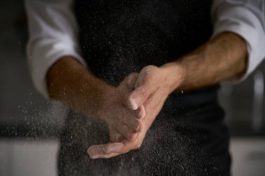 The hands of the strong man knead the dough from which they will make bread, pasta, cake or pizza. In his kitchen he carries on the tradition of homemade pasta. A cloud of white flour flies like dust. clipart