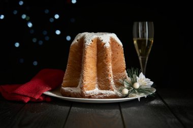 Pandoro, Noel 'i kutlamak için tipik bir İtalyan pastası. Pasta siyah ahşap bir masanın üzerinde bir bardak köpüklü şarap, Noel süslemeleri ve koyu bir arka planda bokeh etkisi var..