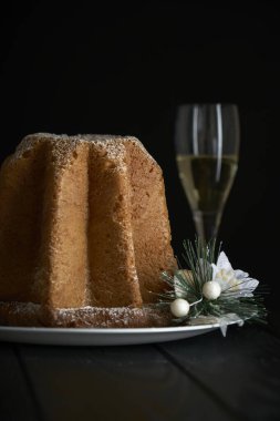 Pandoro, Noel 'i kutlamak için tipik bir İtalyan pastası. Pasta siyah ahşap bir masanın üzerinde bir bardak köpüklü şarap, Noel süslemeleri ve koyu bir arka planda bokeh etkisi var..