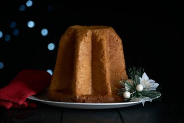 Pandoro, Noel 'i kutlamak için tipik bir İtalyan pastası. Pasta siyah ahşap bir masanın üzerinde bir bardak köpüklü şarap, Noel süslemeleri ve koyu bir arka planda bokeh etkisi var..