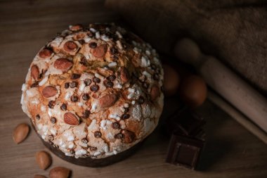 Panettone, tipik İtalyan noel pastası. Çikolata ve bademli. Arka planda panettone, yumurta, un ve çikolata yapımında kullanılan malzemeler var..