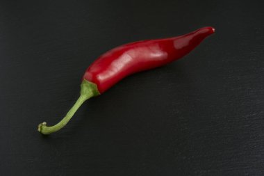 Siyah taş arka planda izole edilmiş kırmızı acı biber, baharatlı ve tutkulu tarifler için ideal malzeme.