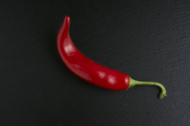 Siyah taş arka planda izole edilmiş kırmızı acı biber, baharatlı ve tutkulu tarifler için ideal malzeme.