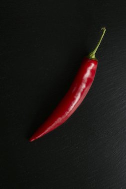 Siyah taş arka planda izole edilmiş kırmızı acı biber, baharatlı ve tutkulu tarifler için ideal malzeme.