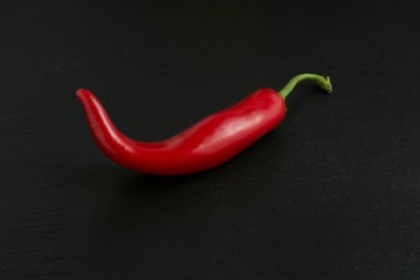 Siyah taş arka planda izole edilmiş kırmızı acı biber, baharatlı ve tutkulu tarifler için ideal malzeme.
