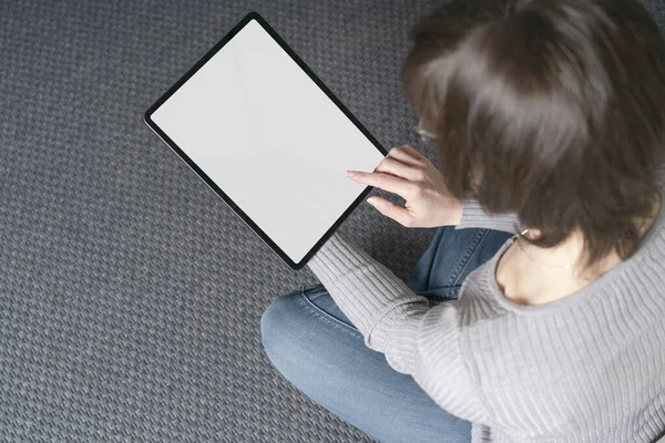 Template mockup tablet with white screen. A young woman use the tablet pc for socialize and shopping online on the sofa at home.