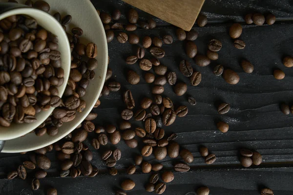 黒コーヒー豆のローストで満たされたセラミックカップ 紙袋と暗いテーブルの上に散乱コーヒー豆と黒の木の板に撮影 ストックフォト