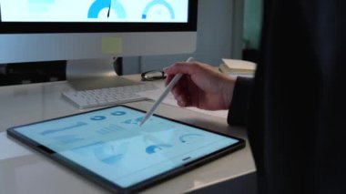 Tablet bilgisayarda çalışan güzel bir iş kadını beyaz masasındaki pazarlama raporunu kalem kullanarak analiz ediyor.