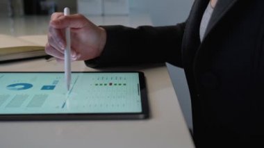 Tablet bilgisayarda çalışan güzel bir iş kadını beyaz masasındaki pazarlama raporunu kalem kullanarak analiz ediyor.