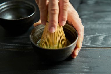 Japon organik kibrit yeşil çayı kasede Chashaku kaşığı ve siyah ahşap arka planda Chasen bambu çırpısı. Japon geleneğinin tipik doğal ürünü. Çay töreni..