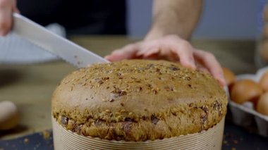 Adamın biri ev yapımı mısır gevreği panettonunu kesiyor ve gösteriyor. Pasta un, yumurta, mısır gevreği, yulaf, hecelenmiş, arpa ve çikolatadan yapılır. Panettone geleneksel İtalyan Noel tatlı ekmeğidir..