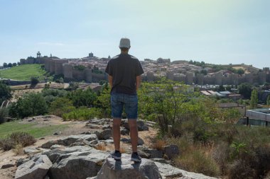 İspanya 'da güneşli bir günde Avila' nın duvarlarını izleyen kısa pantolonlu genç adam.