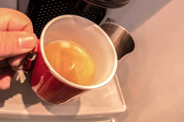 Kahve makinesinden taze demlenmiş bir fincan espresso alan kişinin seçici odak noktası.