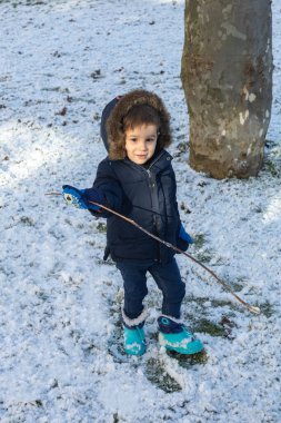 Soğuk bir kış günü, sıcak, sadece botlarıyla kar ve sopayla oynayan bir çocuğun seçici odağı.