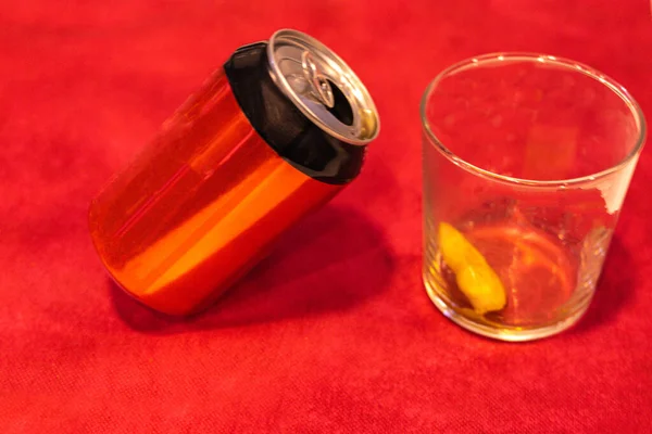 Kırmızı arka planda buzlu ve limonlu kristal bardakla yan yana duran kırmızı ve siyah bir soda kutusunun seçici odağı.