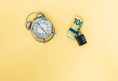 elastik bant, asma kilit ve analog saat ile tutulan birkaç rulo banknotun seçici yaklaşımı kopyalama alanı ile zamanı gösteren bir analog saat ve sarı fon kavramı para